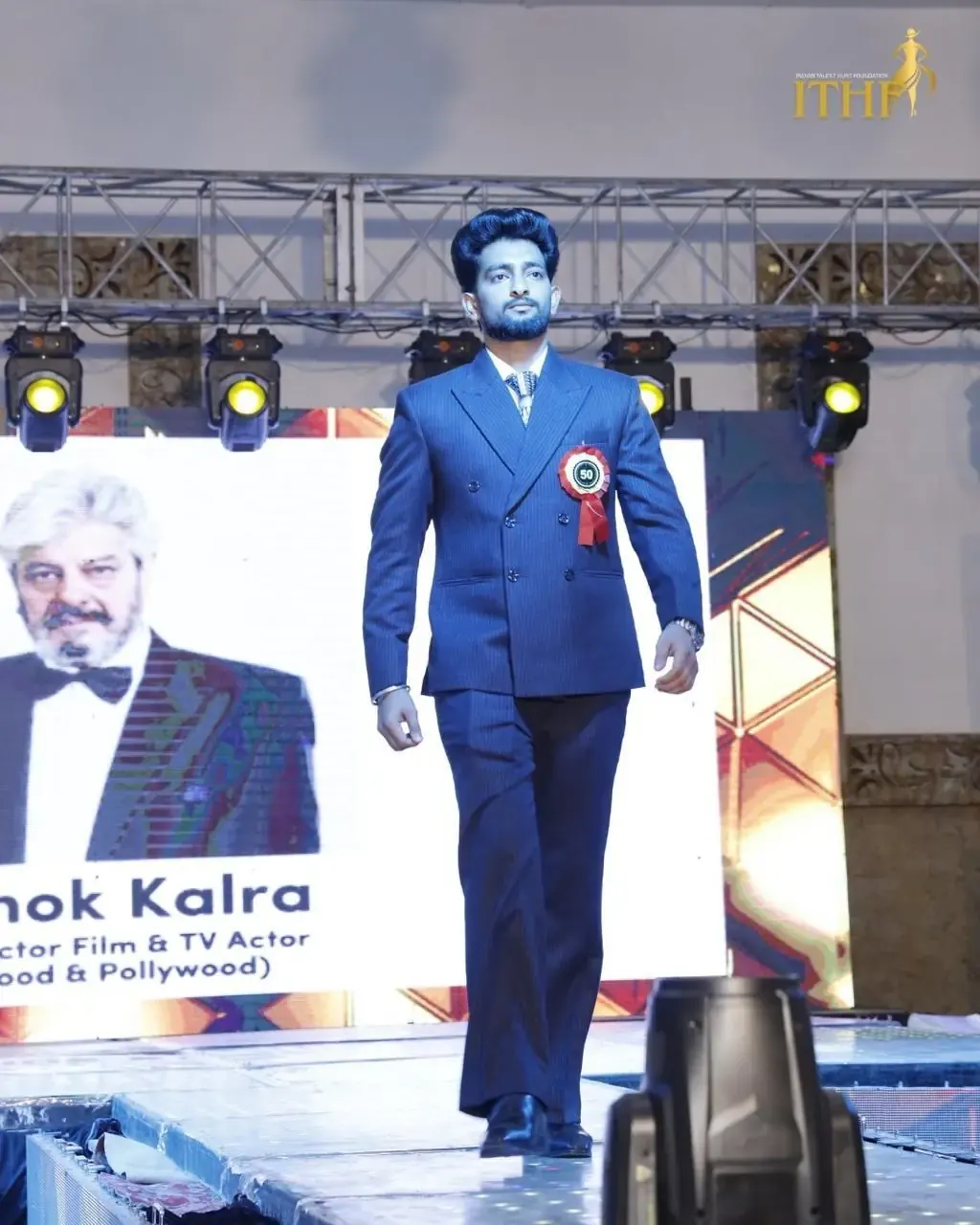 A contestant in a blue suit walking the ramp under stage lights