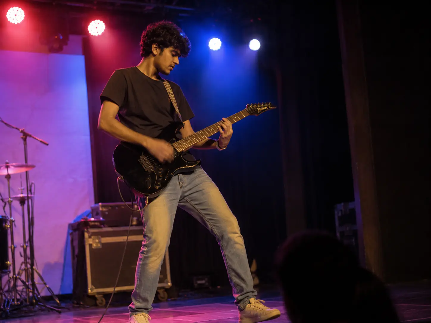 A young guitarist mid-solo on stage under red and blue lights